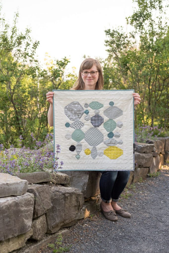 Astrid Bordush holding grey and teal "River Rocks" mini quilt